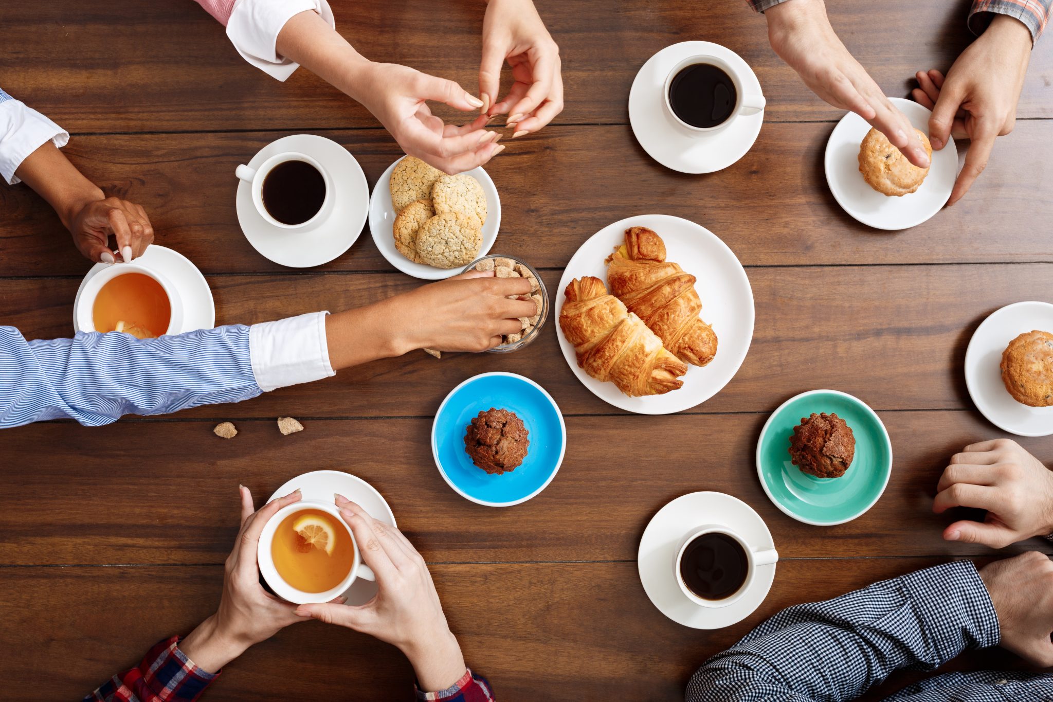 Picture of people's hands on wooden table with croissants and coffee.
